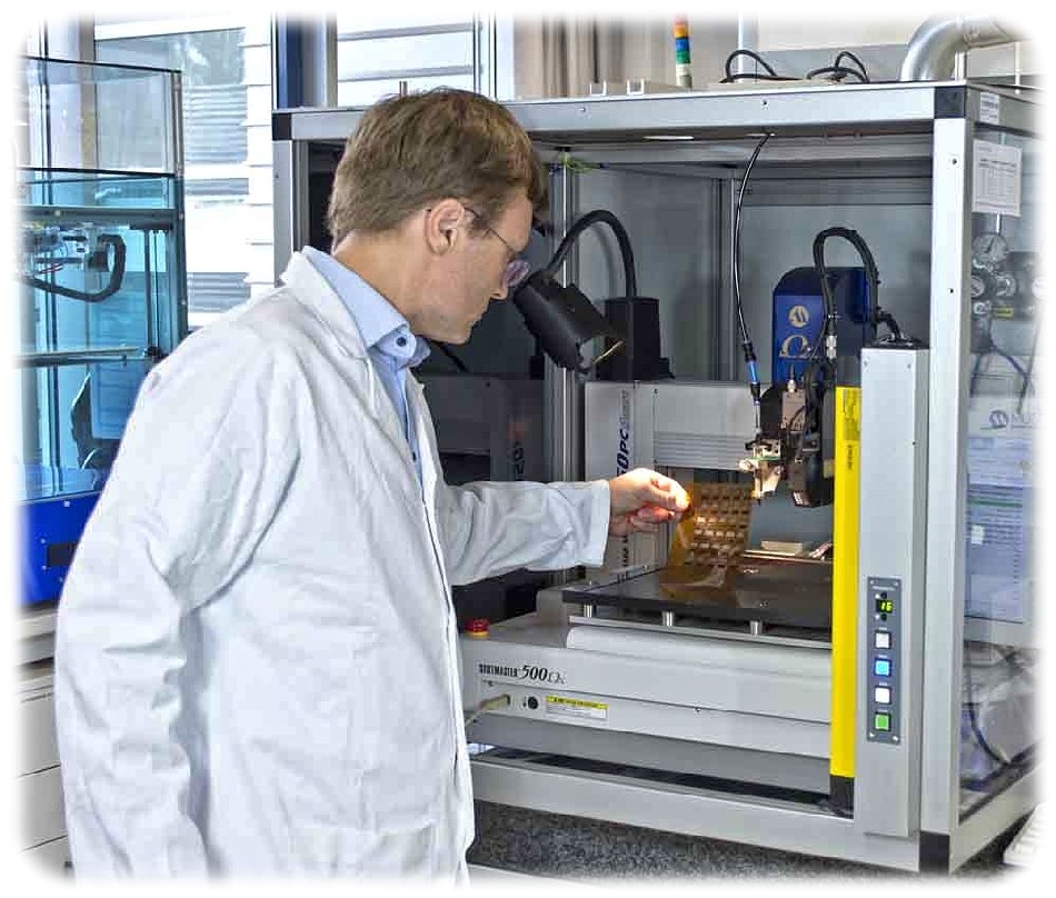 Dr. Roman Tkachov begutachtet an einem Dispensdrucker im Fraunhofer IWS Dresden eine Folie, die er mit zwei verschiedenen leitenden Polymeren bedruckt hat. »PEDOT:PSS« ist ein Polymer mit positiven Ladungsträgern (»p-leitend«), während »Poly(Kx[Ni-itto])« negative Ladungsträger transportiert (»n-leitend«). Dies zeigt auch: Die Polymere des IWS lassen sich mit Standard-Techniken wie Druckern oder Rotationsbeschichtung verarbeiten. Foto: Fraunhofer-IWS Dresden