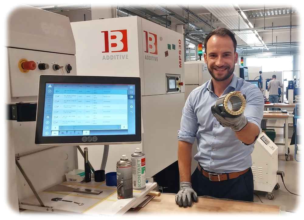 Vertriebs-Geschäftsführer von Additive Drives Philip Arnold zeigt einen Elektromotor, dessen Komponenten teilweise von 3D-Druckern (links im Bild) erzeugt worden sind. Foto: Heiko Weckbrodt