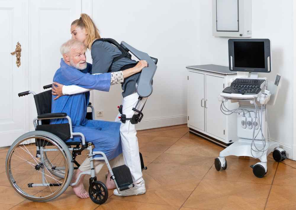Eine Pflegerin hilft mit der Kraftunterstützung eines Exia-Exoskeletts einem Senior aus dem Rollstuhl.  Foto: German Bionic