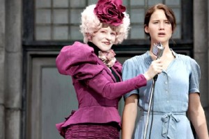 Effie (Elizabeth Banks, links) kommt aus dem Capitol nach Distrikt 12, um für die Todesspiele Kinder zu erlosen. Als ihre Schwester gewählt wird, meldet sich Katniss (Jennifer Lawrence) statt ihrer freiwillig. Foto: Lionsgate