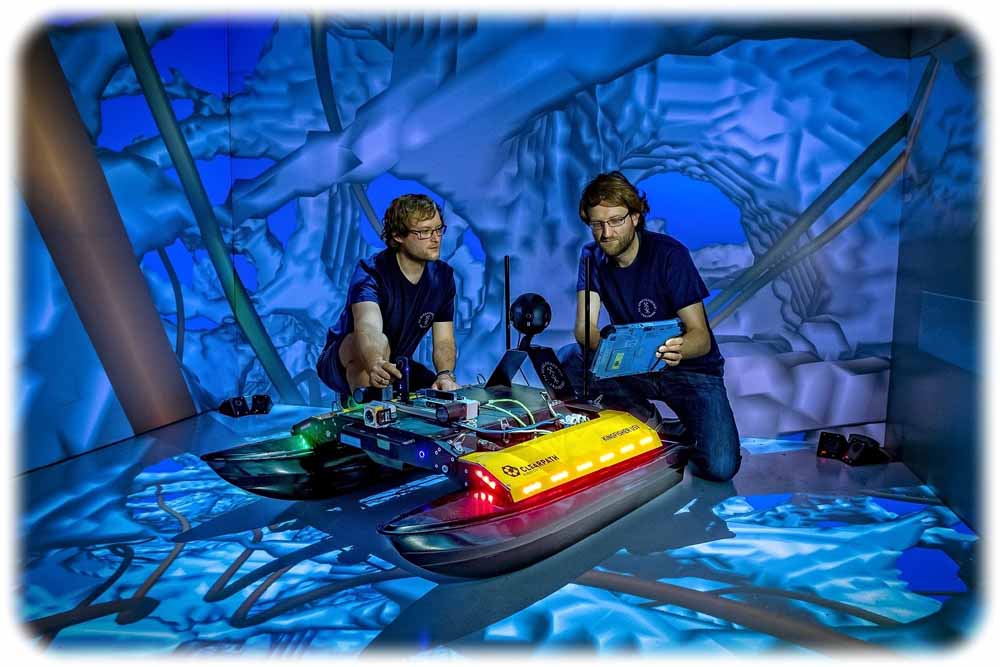 Zwei Freiberger Informatiker arbeiten an dem neu entwickelten Schwimmroboter „Elisabeth“ in einer Forschungs-Höhle für virtuelle Realität, "CAVE" genannt. Foto: Detlev Müller / TU Bergakademie Freiberg
