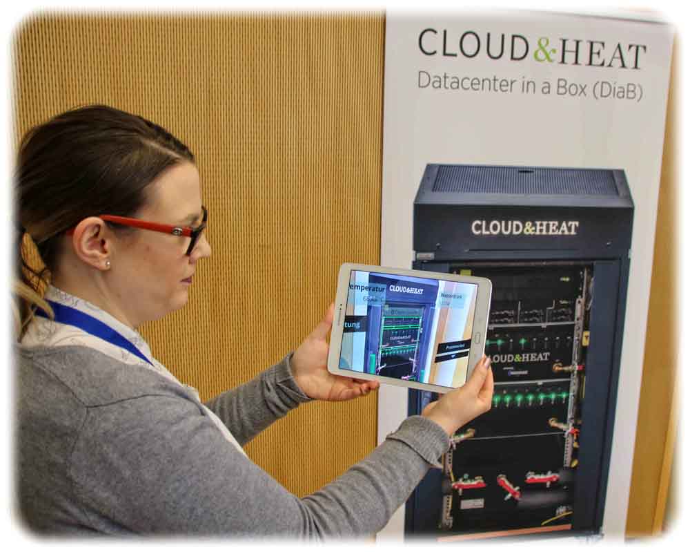 „Cloud & Heat“-Sprecherin Franziska Leitermann zeigt, wie die "Erweiterte Realität" dem Wartungstechniker im Rechenzentrum helfen kann, defekte Prozessor-Stacks zu finden (hier im Beispiel von der KI grün eingerahmt), sich Kühltemperatur, Auslastung oder auch Handbücher digital anzeigen zu lassen. Beim Demonstrator zum FAST-Clustertreffen war es noch ein Tablet, in Zukunft soll die AR per Datenbrille angezeigt werden. Foto. Heiko Weckbrodt