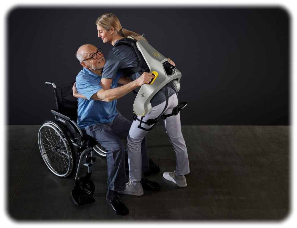 Eine Frau hebt einen Senior mit einem Apogee-Exoskelett aus einem Rollstuhl. Foto: German Bionic