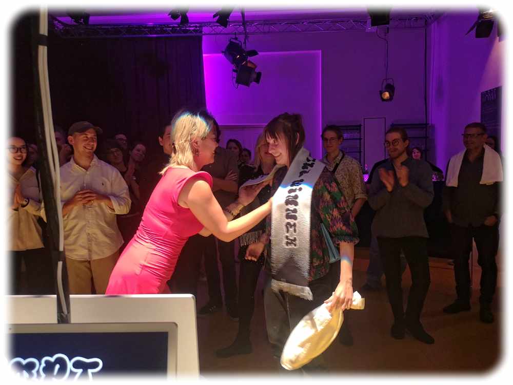Die KI-Fee überreicht der Gewinnerin Kim Rasche die Siegertrophäe der "Prompt Battle". Foto: Heiko Weckbrodt