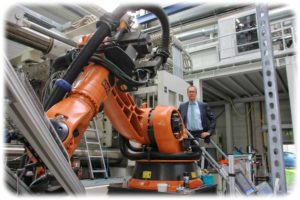 Prof. Maik Gude zeigt im ILK-Technikum einen Roboter, der den Spezialmaschinen Hutablagen aus wiederverwerteten Faserverbundstoffen reicht. Foto: Heiko Weckbrodt