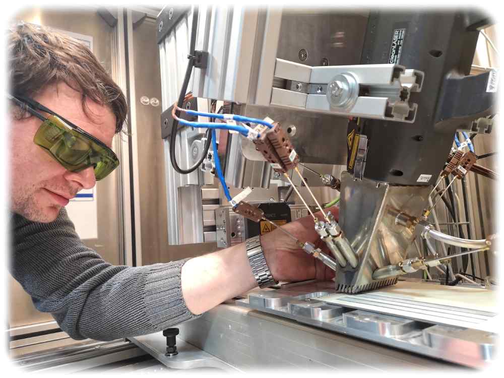 Techniker Erik Findeisen positioniert Thermoelemente an einem Laserkopf im Laserlabor des Instituts für Energietechnik an der TU Dresden. Darunter ist eine lackierte Probe zu sehen, die den Schutzanstrichen in alten Kernkraftwerken ähnelt. Foto: Heiko Weckbrodt