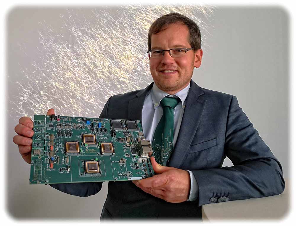 Professor Christian Mayr, Leiter der Professur für Hochparallele VLSI-Systeme und Neuromikroelektronik an der TU Dresden, mit einer Platine, auf die Spinnaker2-Prototypenchips aufgelötet sind. Foto: Heiko Weckbrodt