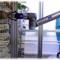 Ein vom STFI abgelernter Roboter von "Universal Robots" bestückt das Spulengatter einer Webmaschine. Bildschirmfoto (hw) aus de Präsentation "Robotik in der Textilfabrik der Zukunft", STFI