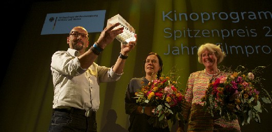 Sven Weser und Jana Engelmann /Mitte) freuen sich über den deutschen Programmkino-Preis, en sich voin Kulturstaatsministerin Monika Grütters  (r.) bekommen haben. Foto: Paveldesign