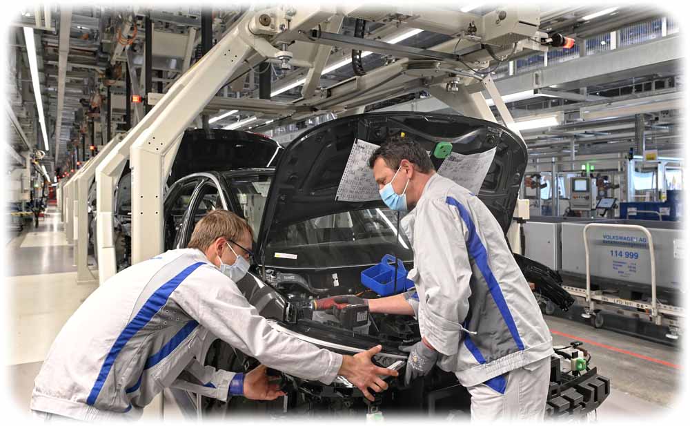Zwei VW-Mitarbeiter tragen Masken und montieren nach der Corona-Pause gemeinsam im Werk Zwickau einen ID3. Foto: Volkswagen Sachsen