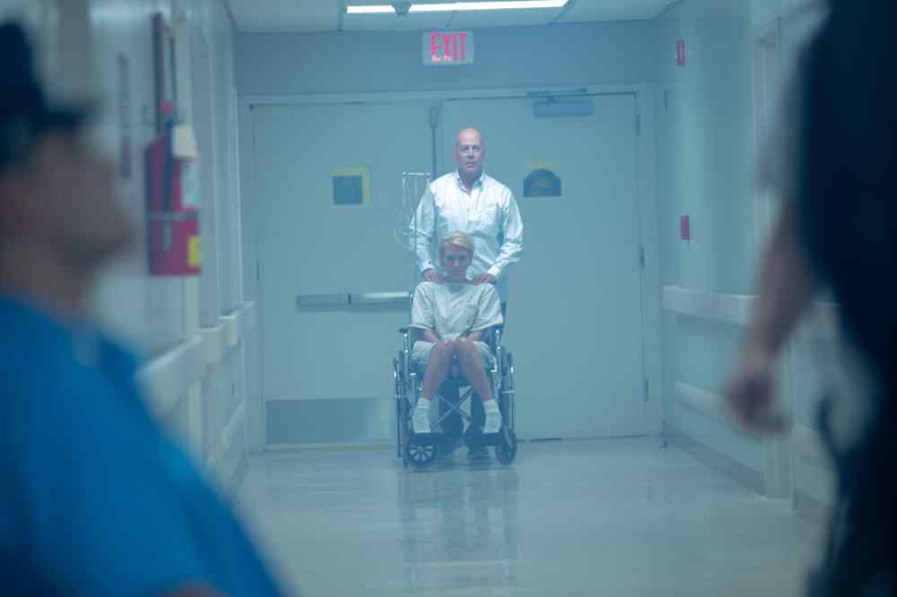 Detective Steve Wakes (Bruce Willis) schiebt seine verletzte Zeugin Madison (Nicky Whelan) im Rollstuhl auf die Seuchenstation, um sie dort zu verstecken. Unterm Strich erweist sich das als keine gute Idee. Szenenfoto (Eurovideo) aus: "Trauma Center"